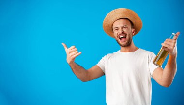 Mavi arka planda bira şişesi tutan tişörtlü neşeli genç adam.