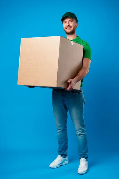 Delivery man with box in studio against blue background