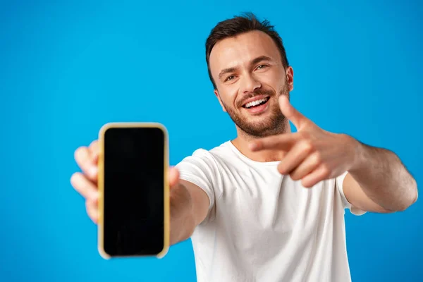 Yeni akıllı telefonun reklamını yapan genç adamın portresi, onu mavi arka planda kameraya gösteriyor. — Stok fotoğraf