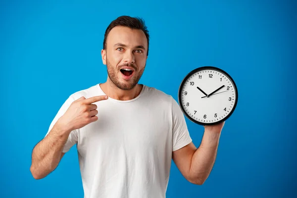 Hezký mladý muž v bílém tričku pózuje s hodinami na modrém pozadí — Stock fotografie