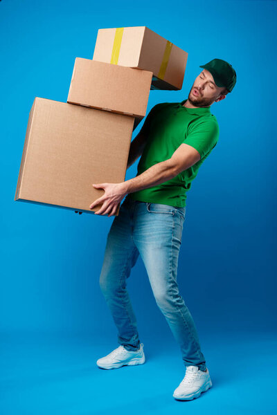 Delivery man with huge pile of boxes against blue background