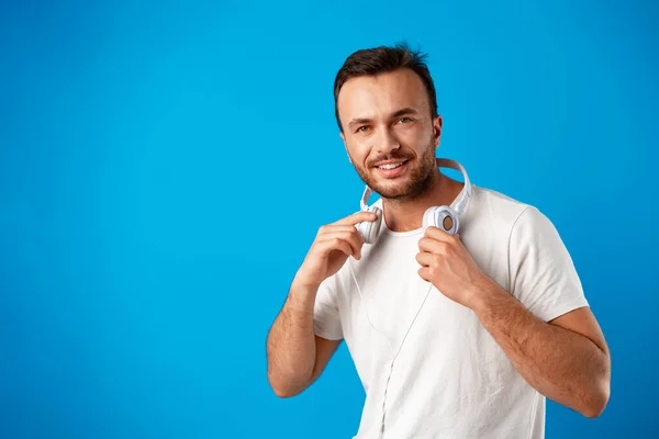 Young man in casual white t-shirt with headphones against blue background — Stock Photo, Image