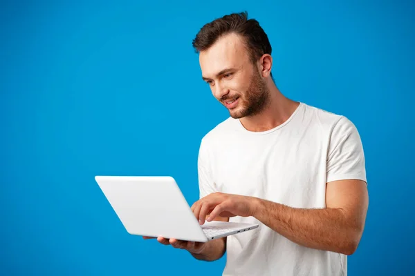 Jóképű fiatalember használja a laptopját a kék háttér — Stock Fotó