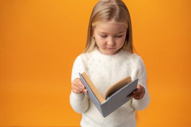 Little beautiful smiling girl holding book against yellow background