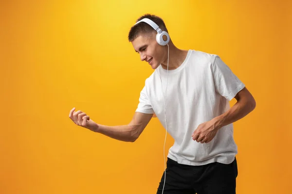 Handsome teenage boy with headphones on head against yellow background — стоковое фото