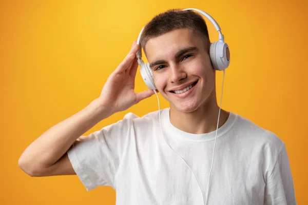 Bonito adolescente com fones de ouvido na cabeça contra fundo amarelo — Fotografia de Stock