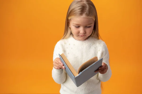 Маленькая красивая улыбающаяся девочка держит книгу на желтом фоне — стоковое фото