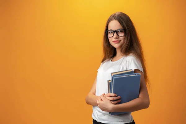 Mądra nastolatka dziewczyna w okularach gospodarstwa książki na żółtym tle — Zdjęcie stockowe