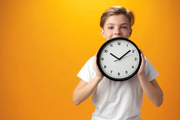 Portrait of a young boy holding a clock against yellow background — 스톡 사진