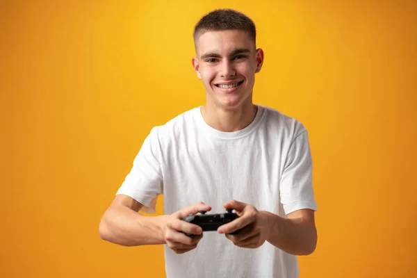 Young man playing computer games with jojystick against yellow background — Fotografia de Stock