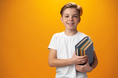 Little schoolboy holding a book against yellow background