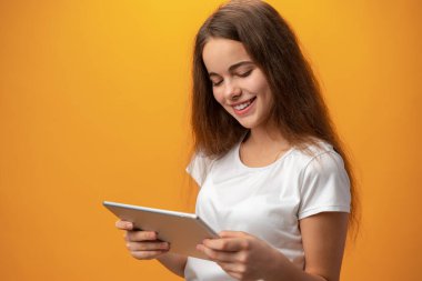 Beautiful teen girl using digital tablet over yellow studio background