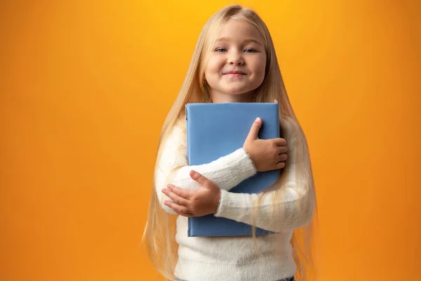Little beautiful smiling girl holding book against yellow background — Zdjęcie stockowe