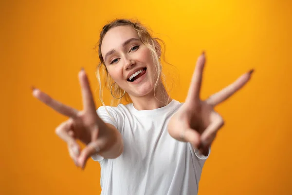 Portrait of a young funny woman showing peace gesture with two hands isolated over yellow background. — Stockfoto