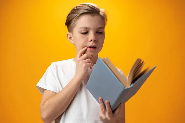 Little schoolboy holding a book against yellow background — Zdjęcie stockowe