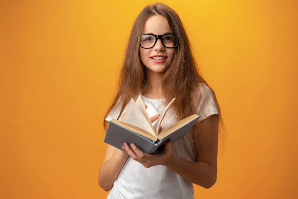 Умная девушка в очках держит книгу на жёлтом фоне — стоковое фото