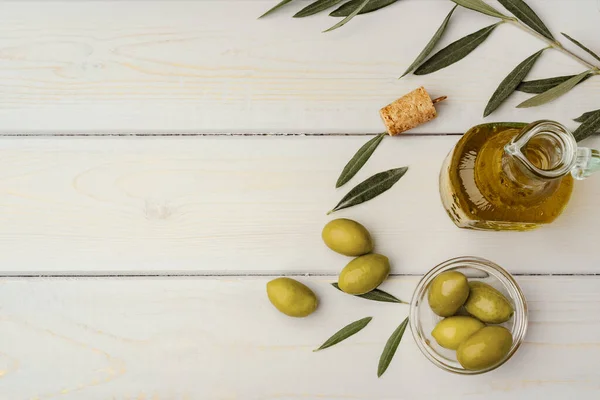 Olijven en fles olijfolie op houten ondergrond — Stockfoto