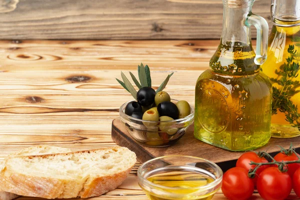 Olijven en fles olijfolie op houten ondergrond — Stockfoto