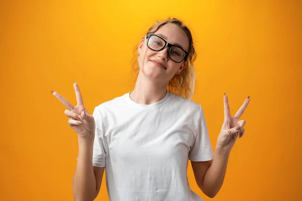 Portrait of a young funny woman showing peace gesture with two hands isolated over yellow background. — Stockfoto