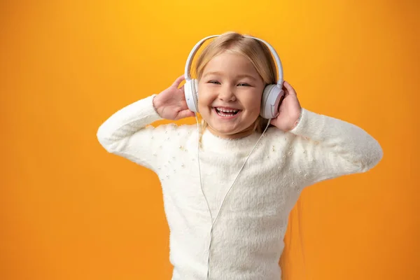 Niña pequeña usa auriculares escucha música sobre fondo amarillo — Foto de Stock