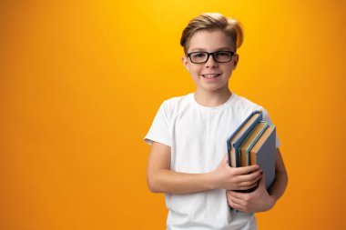 Küçük okul çocuğu sarı arka planda bir kitap tutuyor.