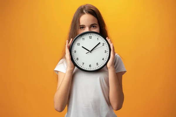 Beautiful teen girl holding wall clock over yellow background — 스톡 사진