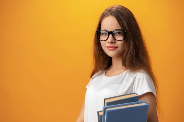 Mądra nastolatka dziewczyna w okularach gospodarstwa książki na żółtym tle — Zdjęcie stockowe