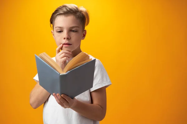 Little schoolboy holding a book against yellow background — Zdjęcie stockowe