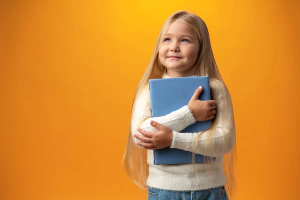 Little beautiful smiling girl holding book against yellow background — Zdjęcie stockowe