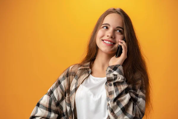 Csinos tizenéves lány beszél a mobiltelefon sárga háttér — Stock Fotó