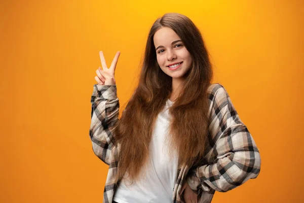 Junge kaukasische Teenagerin zeigt ein Friedenssymbol vor gelbem Hintergrund — Stockfoto