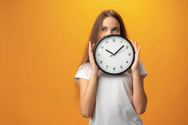 Beautiful teen girl holding wall clock over yellow background — 스톡 사진