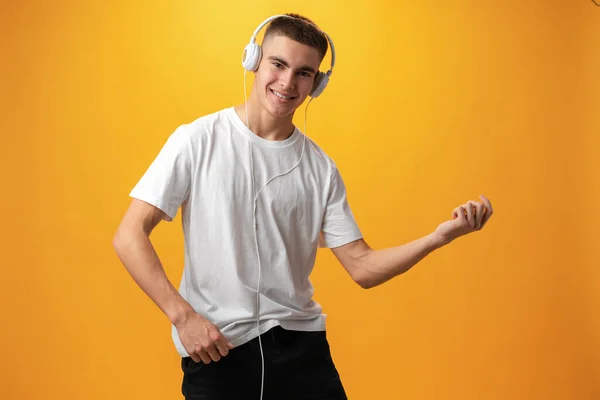 Handsome teenage boy with headphones on head against yellow background — ストック写真