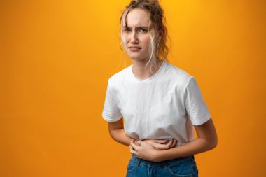Sick young teen woman having a stomach ache against yellow background