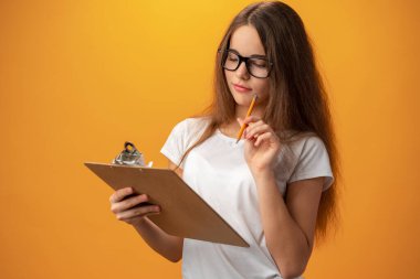 Teen school girl taking notes on clipboard against yellow background