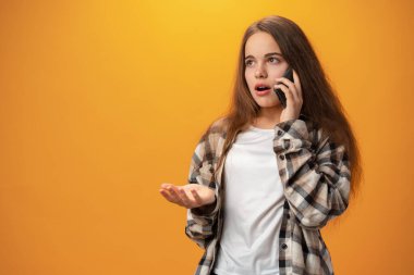 Pretty teenage girl talking on the mobile phone against yellow background