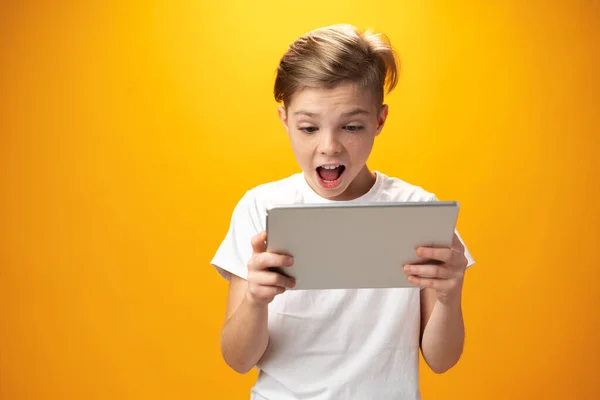 Little boy playing with digital tablet against yellow background — Fotografia de Stock