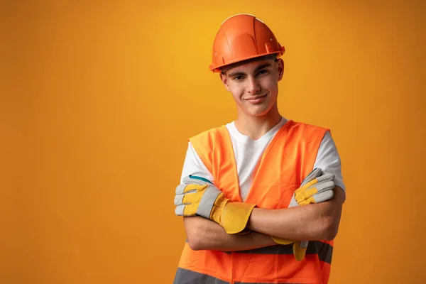 Confident smiling teen boy wearing orange hard hat against yellow background — Stock Fotó
