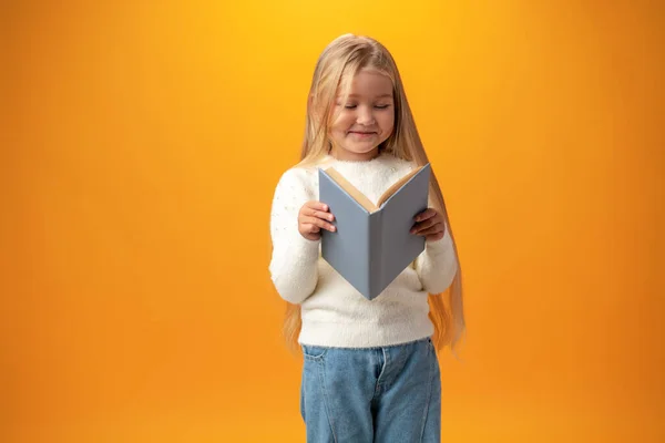 Küçük güzel gülümseyen kız sarı arka planda kitabı tutuyor. — Stok fotoğraf