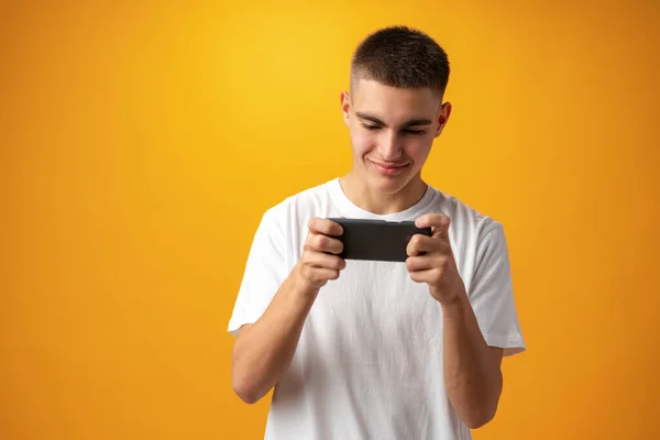 Junger lässiger Mann mit Smartphone vor gelbem Hintergrund — Stockfoto