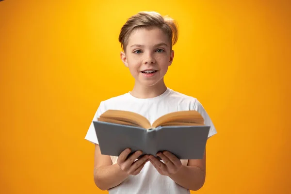 Маленький школьник держит книгу на жёлтом фоне — стоковое фото