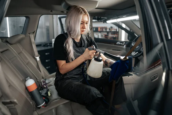 Kobieta sprzątanie salonu samochodowego z lakierowania spray w usłudze szczegółowo samochodu — Zdjęcie stockowe