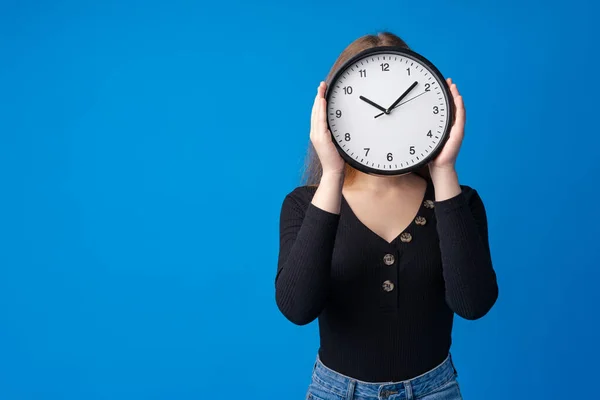 Hermosa chica adolescente sosteniendo reloj de pared sobre fondo azul — Foto de Stock