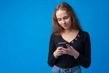 Mavi arka planda akıllı telefon kullanan genç bir kızın portresi