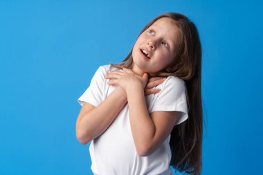 Şok olmuş küçük kız mavi arka planda şaşkınlıkla bakıyor