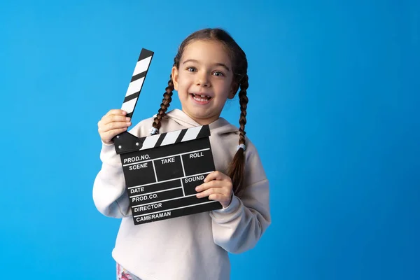 Smiling girl holding clapper board against blue background — Stock Photo, Image