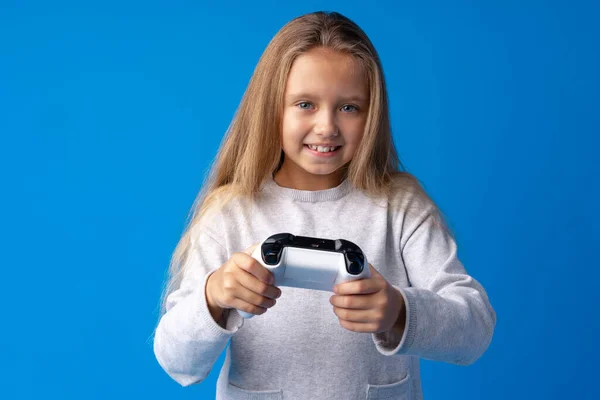 Young cute girl plays computer game with joystick on blue background — Stock Photo, Image