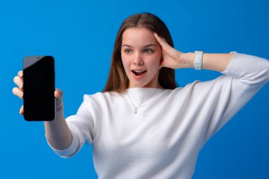 Mavi arka planda boş cep telefonu gösteren gülümseyen bir kadının portresi