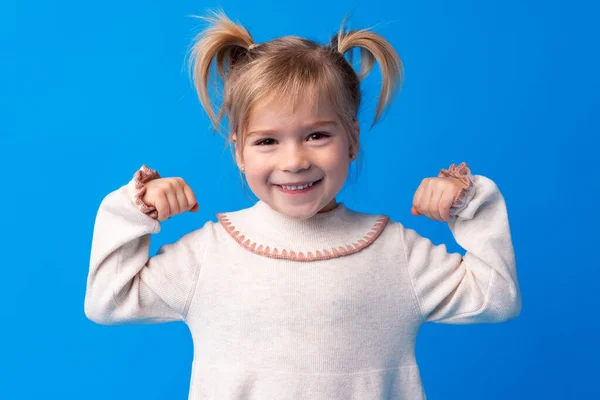 Kicsi aranyos lány mutatja erejét ellen kék háttér — Stock Fotó