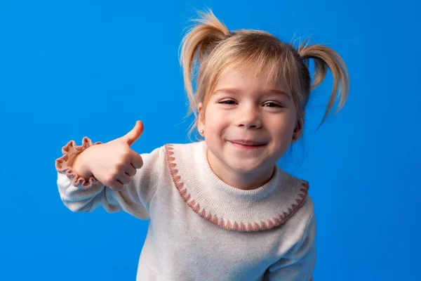 Aranyos kislány mutatja hüvelykujját fel a kék háttér — Stock Fotó
